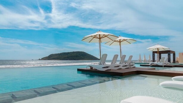 A poolside area with lounge chairs and umbrellas, overlooking a beach and ocean.