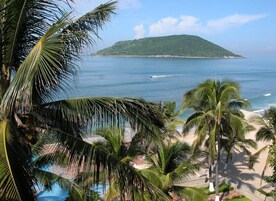 Una playa con palmeras, una piscina y vista a una isla distante.