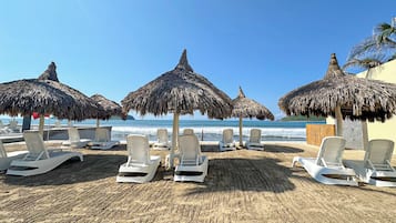 A beach with white lounge chairs and thatched umbrellas, a sandy beach, and the ocean in the background.