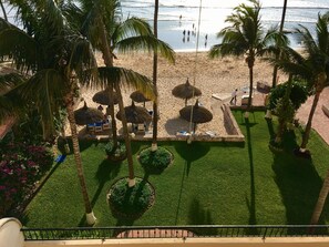 A beach view with palm trees, umbrellas, and a pool area.