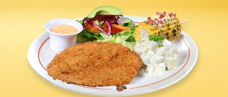 A plate with a breaded cutlet, a salad, a corn on the cob, and a small bowl of sauce.