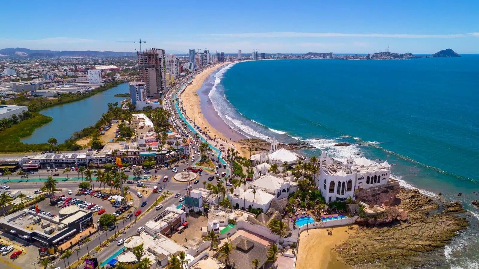 Un paysage urbain côtier avec une plage, un bâtiment historique blanc et un immeuble moderne en construction.