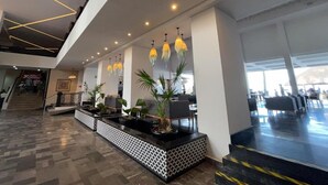A modern lobby with a reception desk, potted plants, and a staircase leading to upper floors.