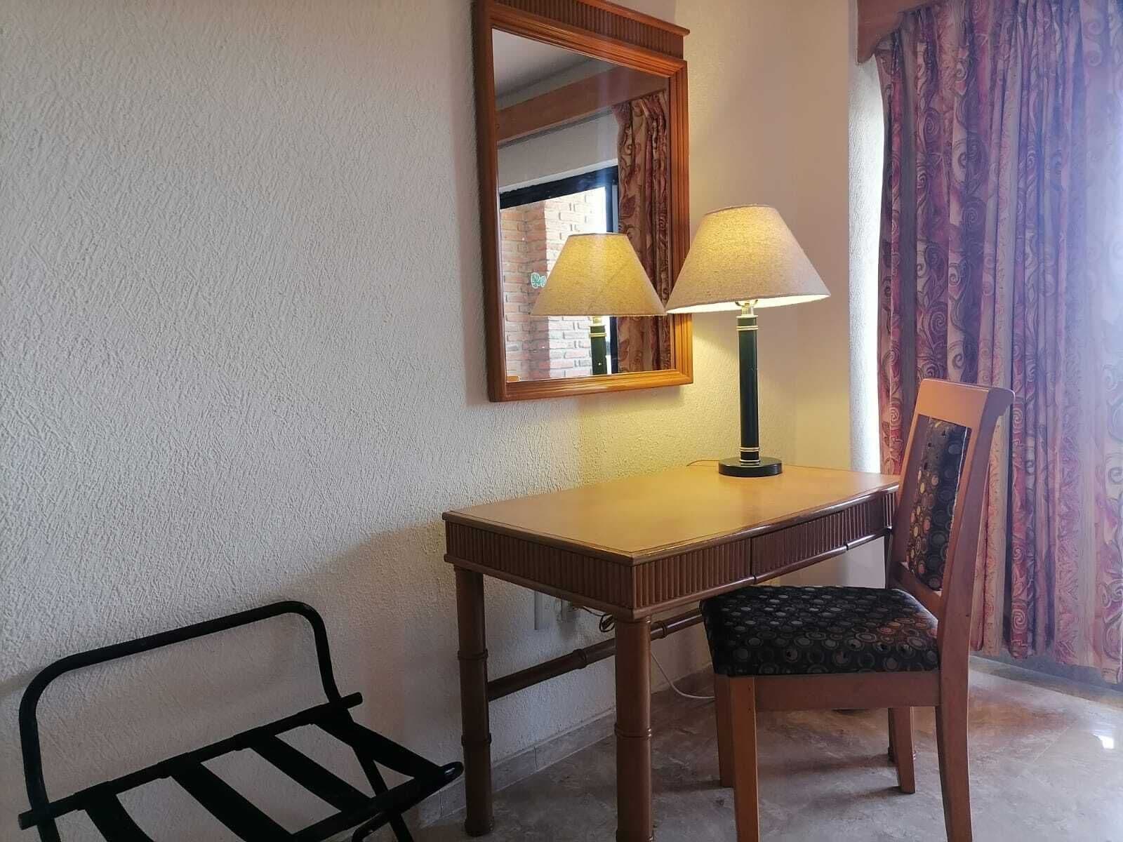Un petit bureau avec une lampe, une chaise et un miroir.