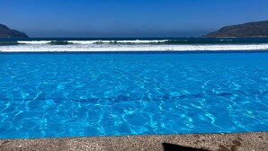 A clear blue pool with a view of the ocean and distant hills.