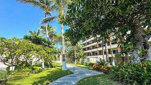 A pathway leading to a building with multiple balconies, surrounded by lush greenery and palm trees.