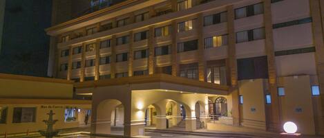 A multi-story hotel with a central courtyard, illuminated by ground lights and a large round light fixture.