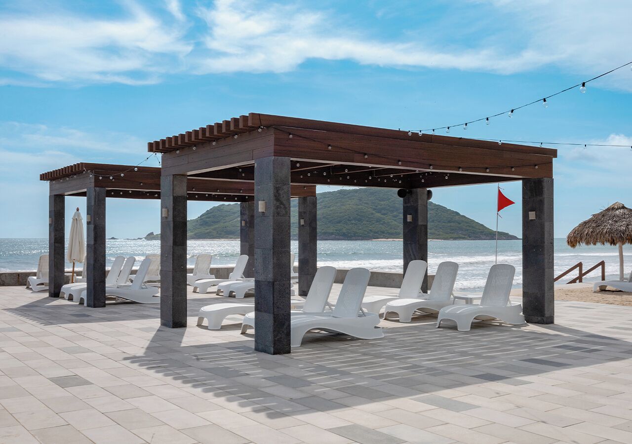 Een strandlounge met witte ligbedden en een houten pergola.