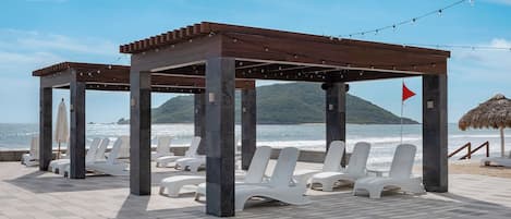 Een strandlounge met witte ligbedden en een houten pergola.