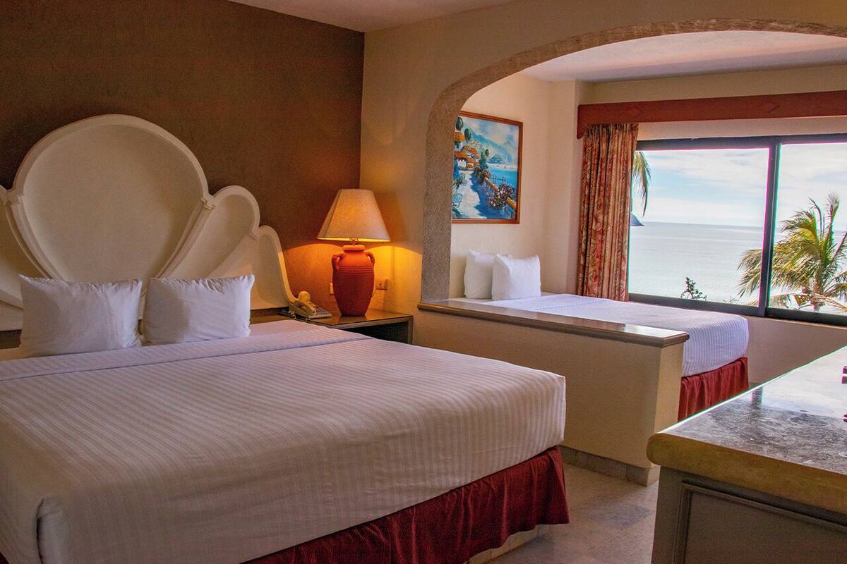 A hotel room with two beds, a desk, a lamp, and a painting.