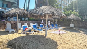 Una playa con sombrillas de paja, sillas de descanso y un muro de piedra.