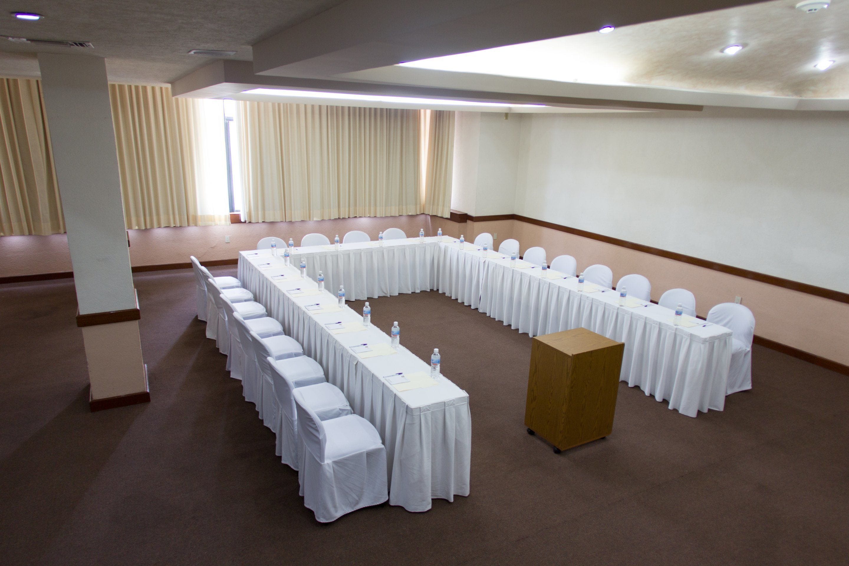Une salle de conférence avec une longue table et des chaises, un pupitre et une grande fenêtre avec des rideaux.