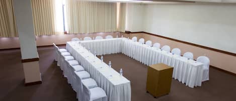 Une salle de conférence avec une longue table et des chaises, un pupitre et une grande fenêtre avec des rideaux.