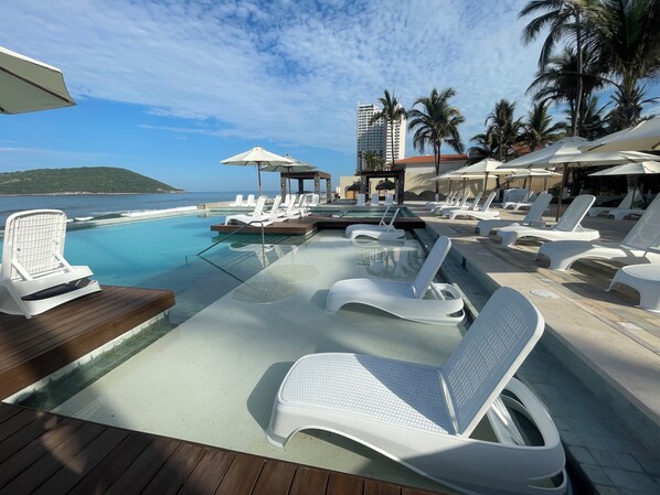 A poolside area with lounge chairs, umbrellas, and a view of the ocean.