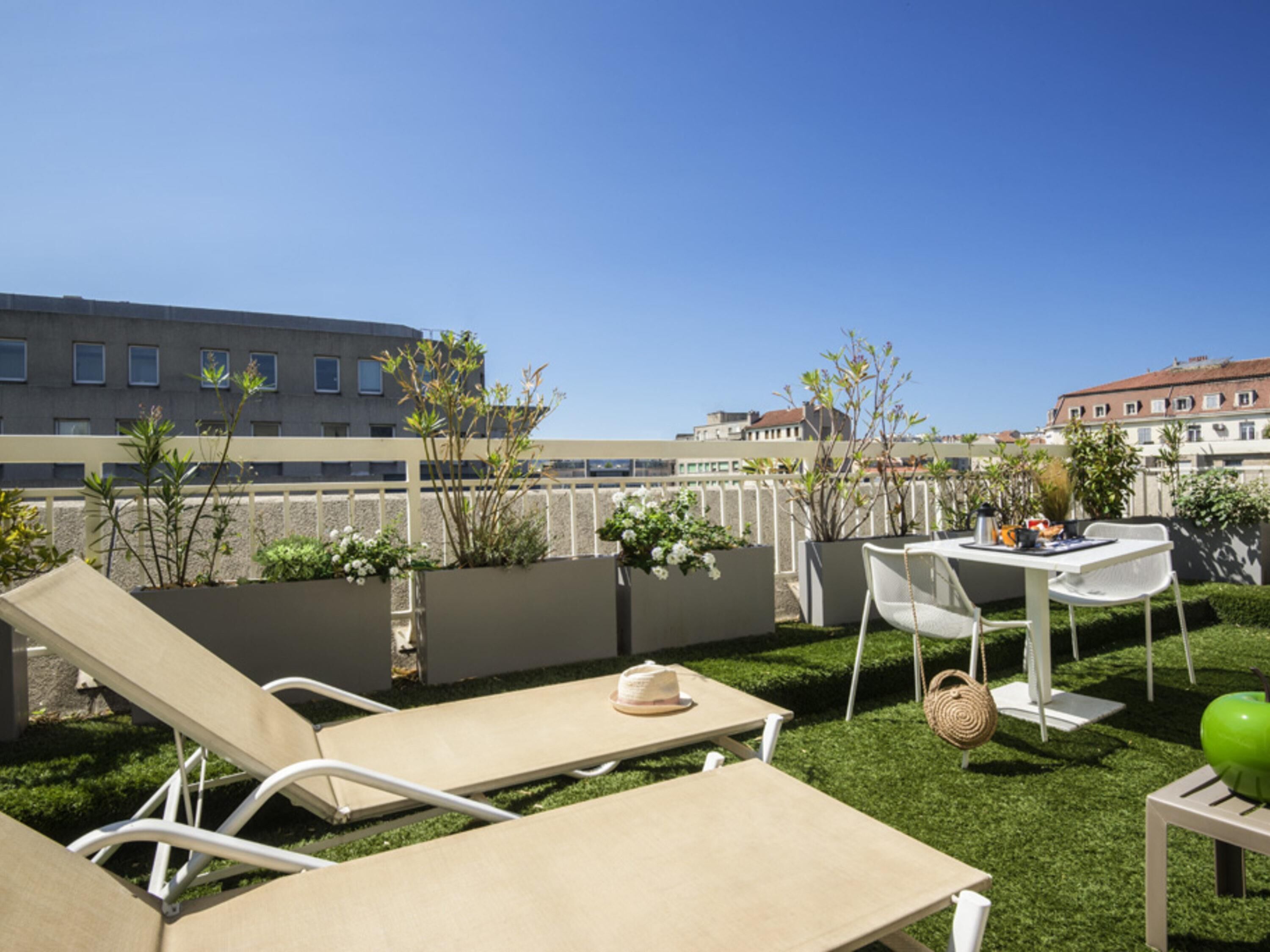 A rooftop terrace with lounge chairs, a table, and potted plants.