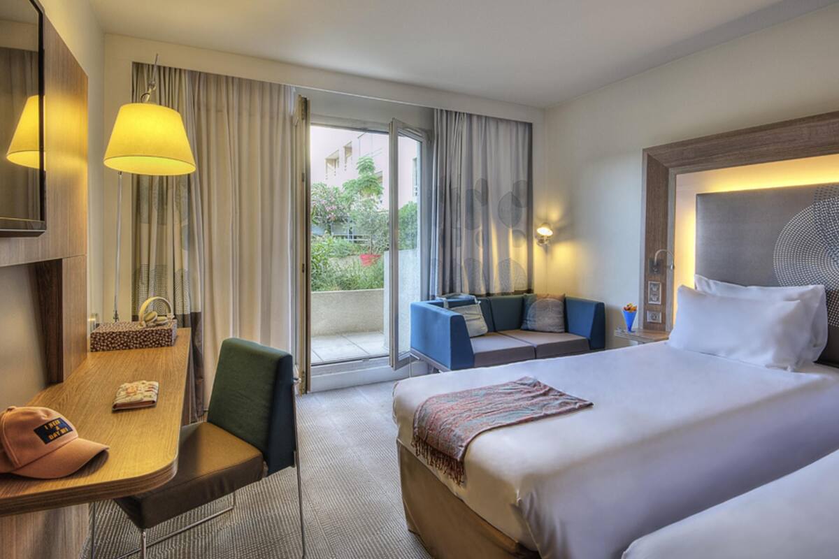 Een hotelkamer met een bed, bureau, stoel, tafel, lamp, raam en uitzicht op het omliggende landschap.