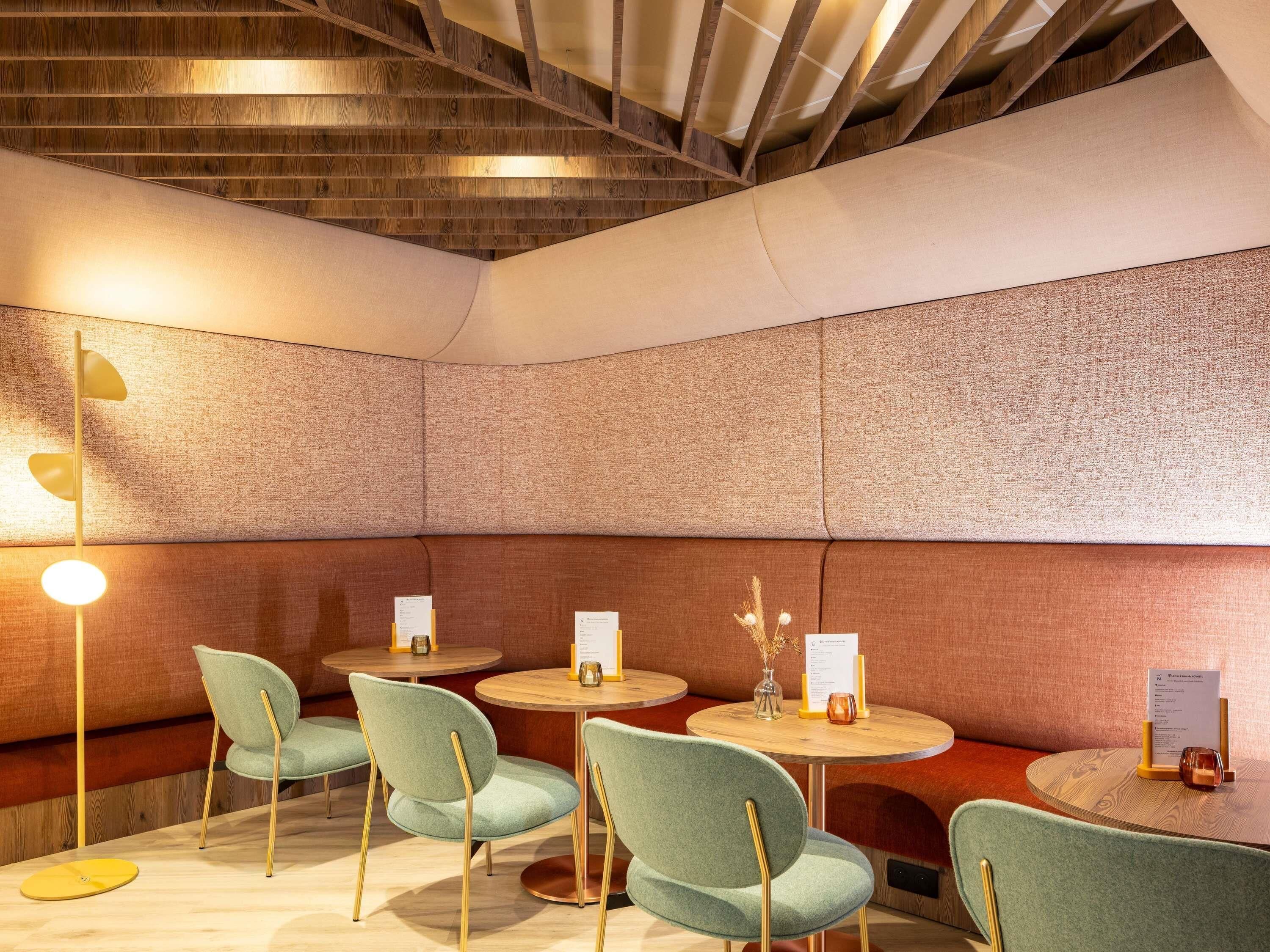 A modern interior with wooden beams, cushioned seating, and round tables.