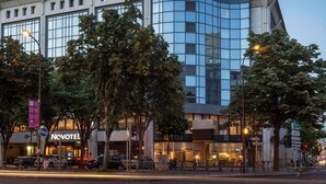 A modern hotel with a glass facade, a visible sign for Novotel, and a street view with parked cars and trees. - Novotel Marseille Centre Prado Vélodrome (Marseille)