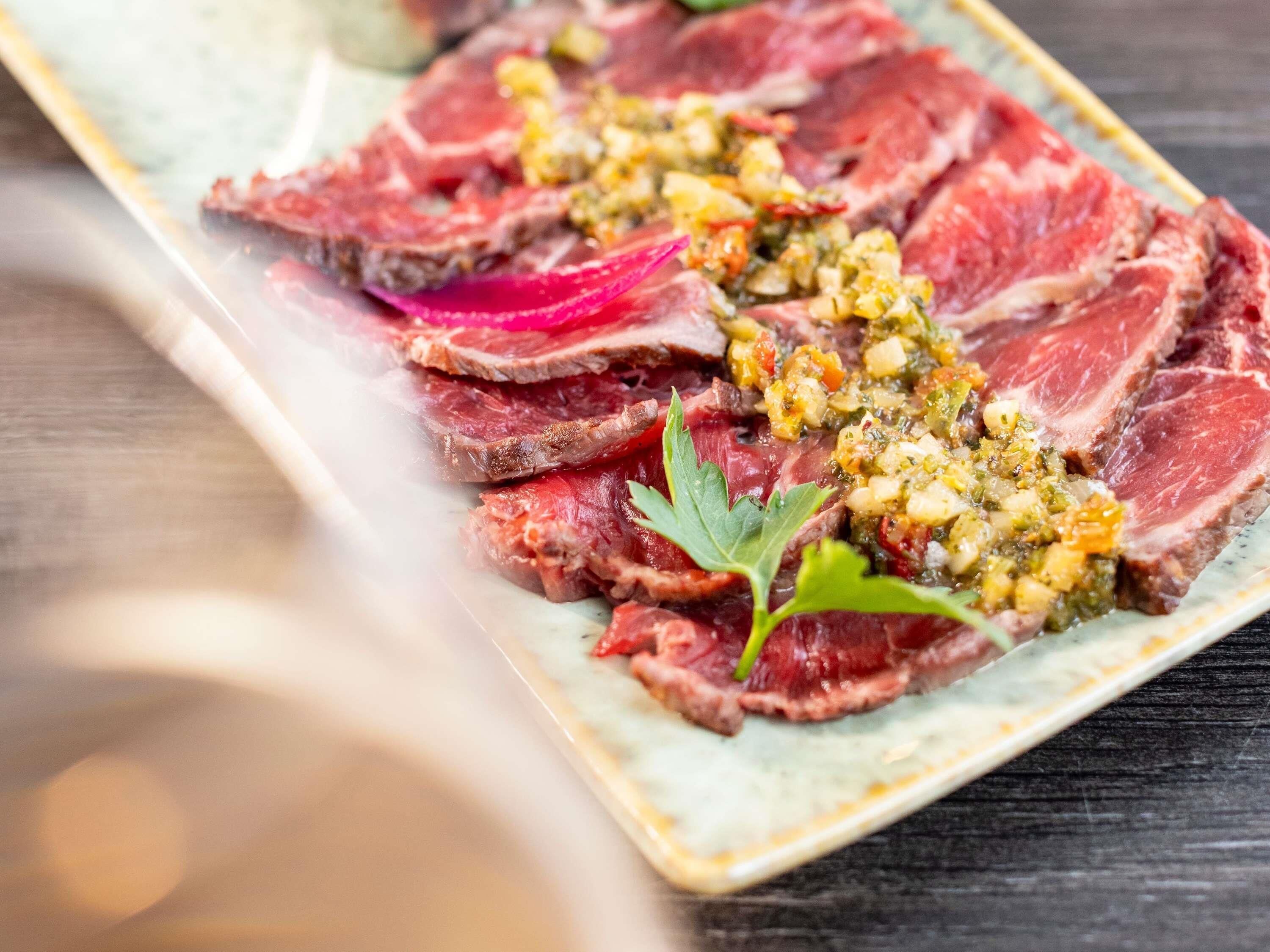 A plate of sliced steak with a herb and vegetable topping.