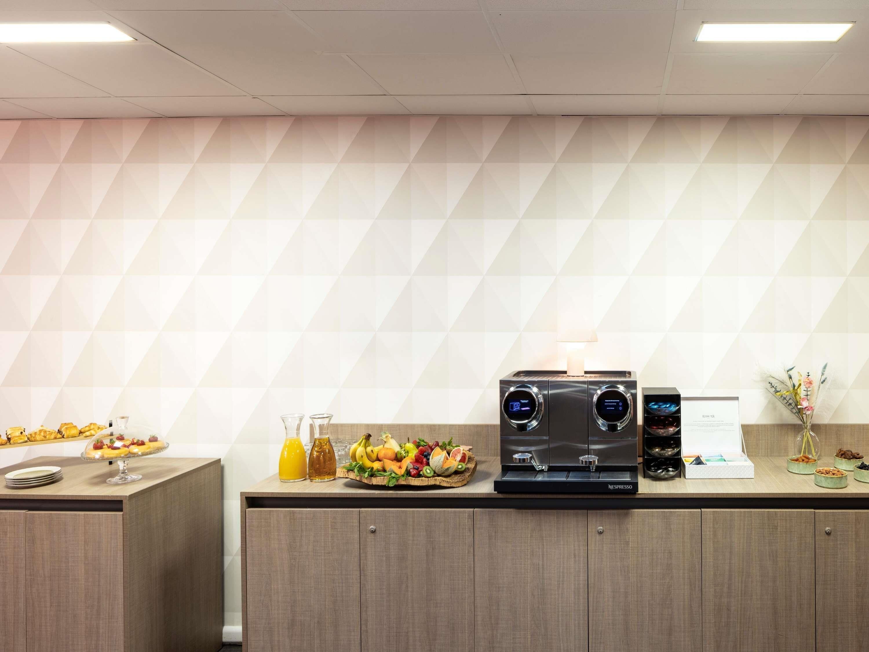 A kitchenette with a coffee machine, fruit display, and a small refrigerator.