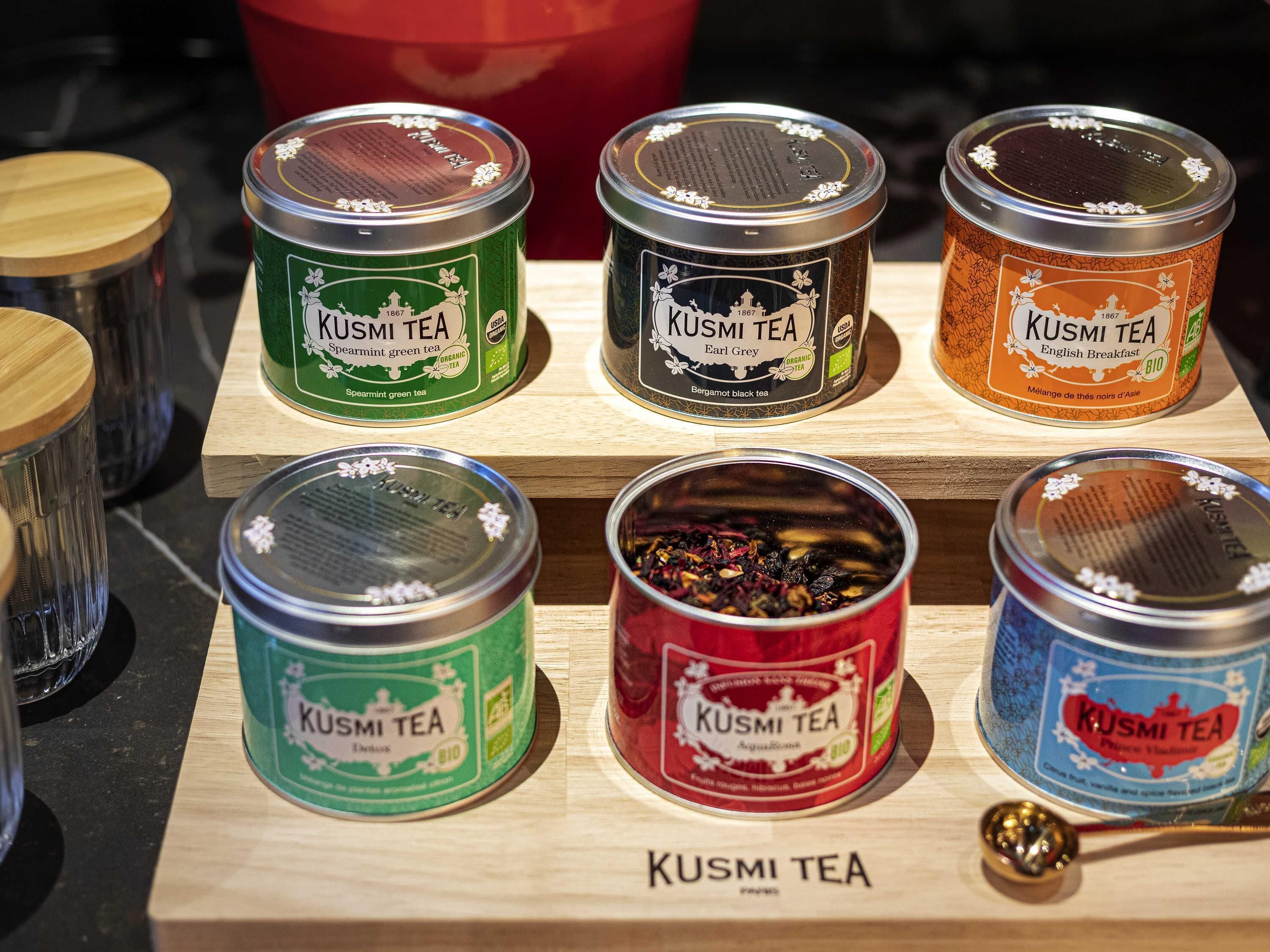 Una selezione di barattoli KUSMI TEA esposti su un ripiano in legno.
