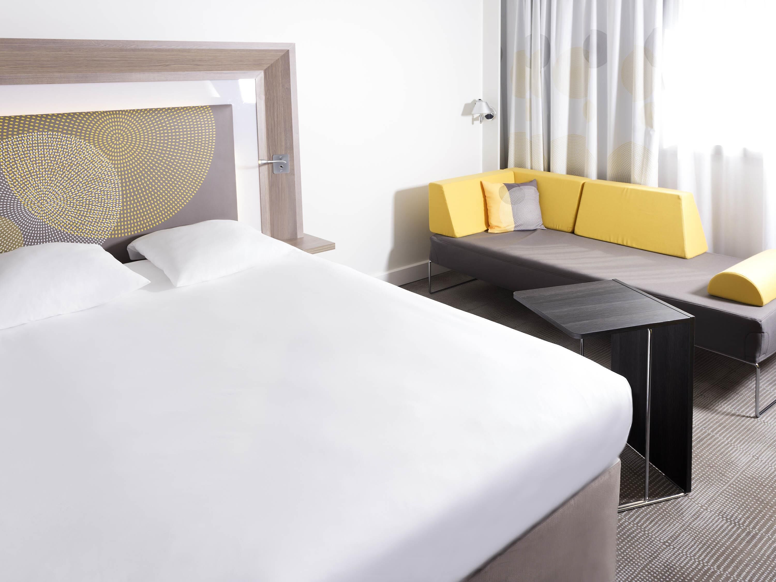 Ein Hotelzimmer mit einem Bett, einer Couch, einem kleinen Tisch und einem Kopfteil mit geometrischem Muster.