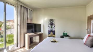 Une chambre d’hôtel avec un lit, un téléviseur posé sur un meuble, un tableau accroché au mur, une valise et une vue sur l’extérieur.
