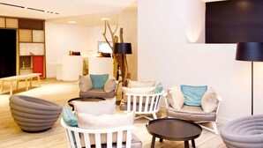 A modern living room with white furniture, a round coffee table, and a large flat-screen TV. - Novotel Marseille Centre Prado Vélodrome (Marseille)