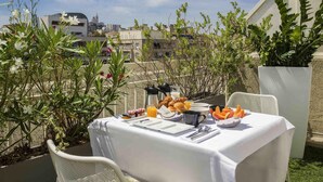 An outdoor dining area with a table set for breakfast, surrounded by greenery and overlooking a cityscape. - Novotel Marseille Centre Prado Vélodrome (Marseille)