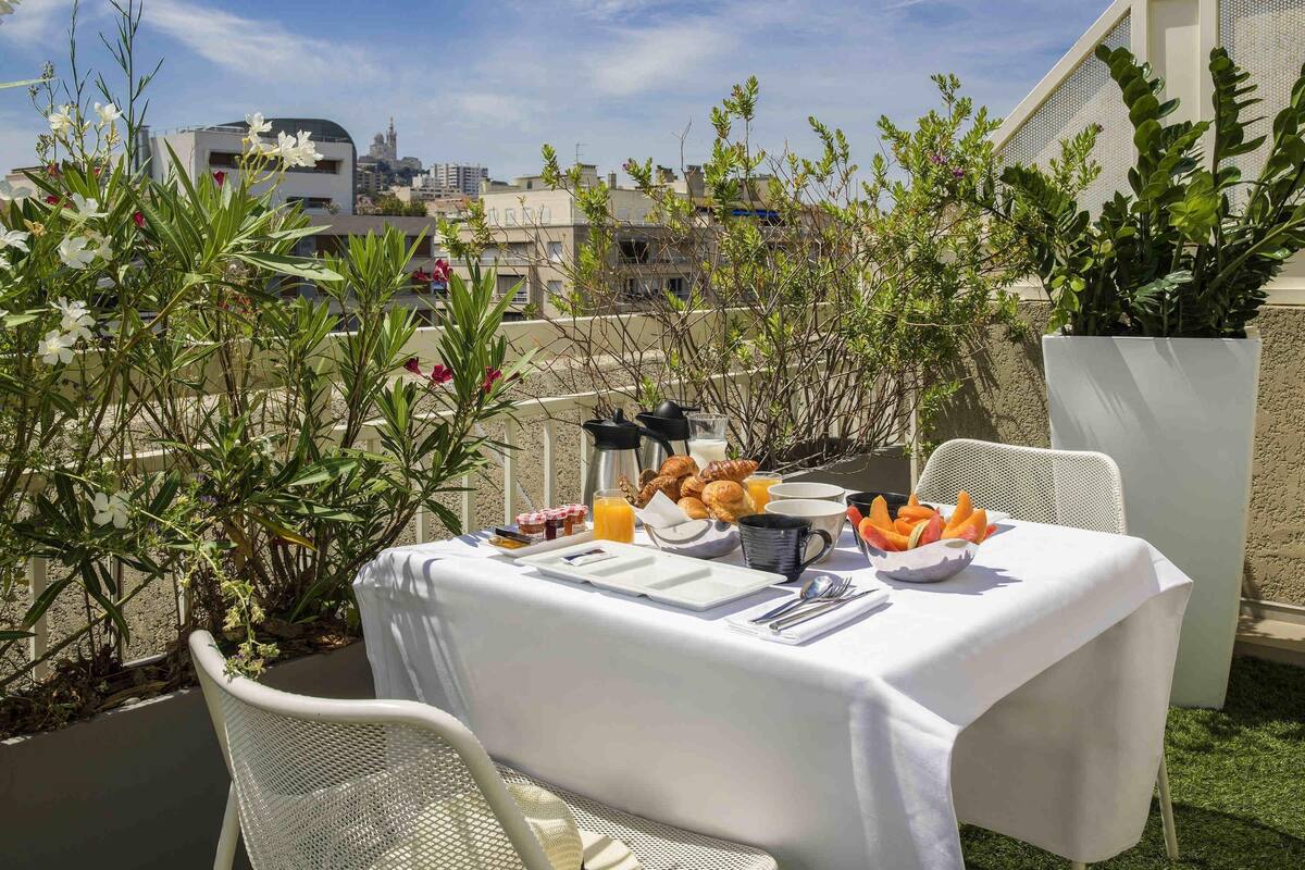 Een terras met een ontbijttafel, omgeven door groen en met uitzicht op een stadsbeeld.
