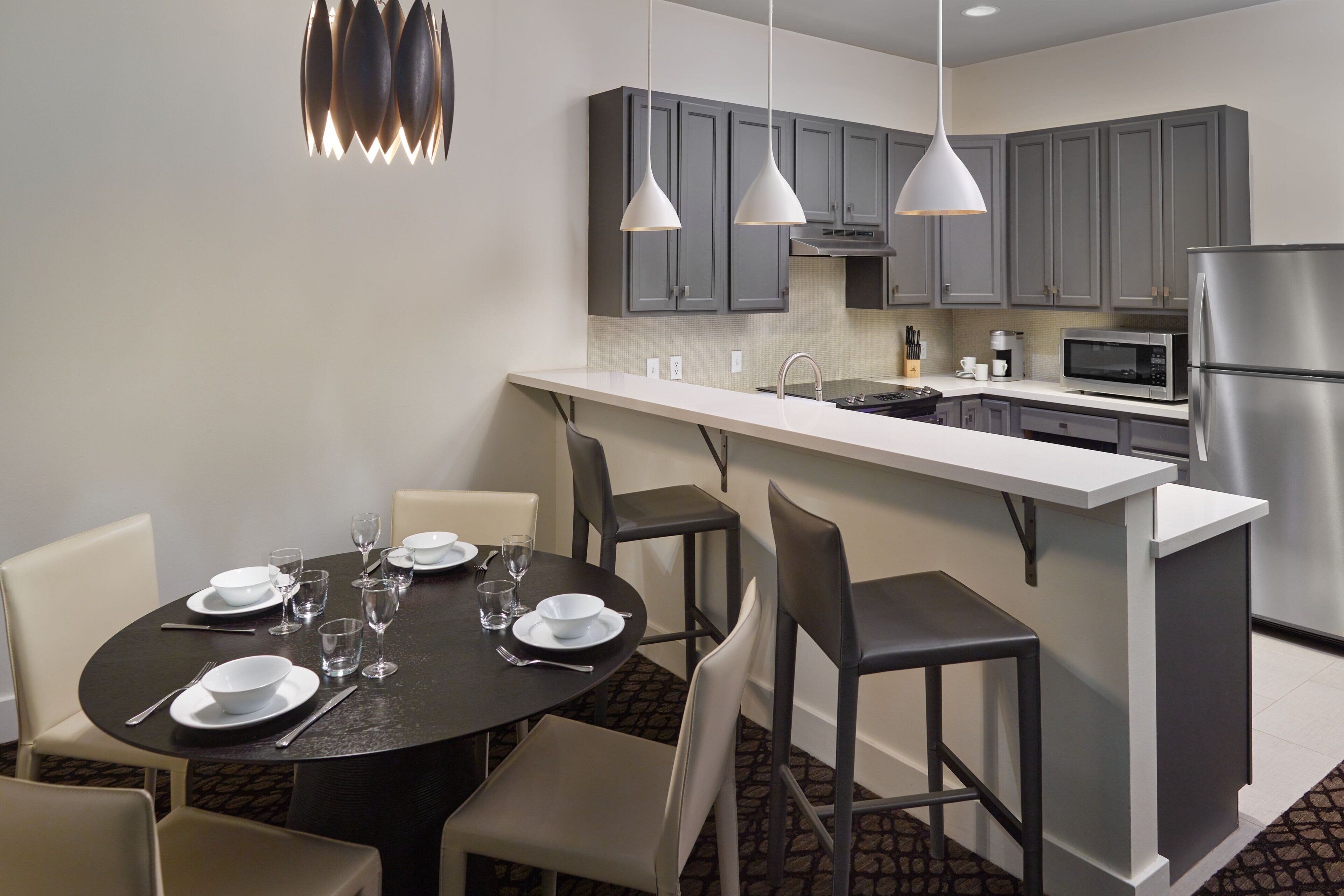 A modern kitchen with grey cabinets, a stainless steel refrigerator, and a dining area with a round table set for four.