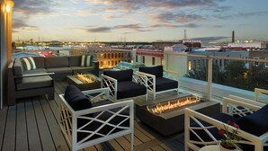 Eine Dachterrasse mit Sitzgelegenheiten im Freien, einem Feuerbereich und Blick auf die Stadtlandschaft.