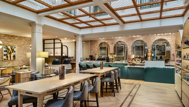 Ein geräumiges Café mit Holztischen und -stühlen, einer Theke mit einer Speisekarte und einer Ziegelwand.