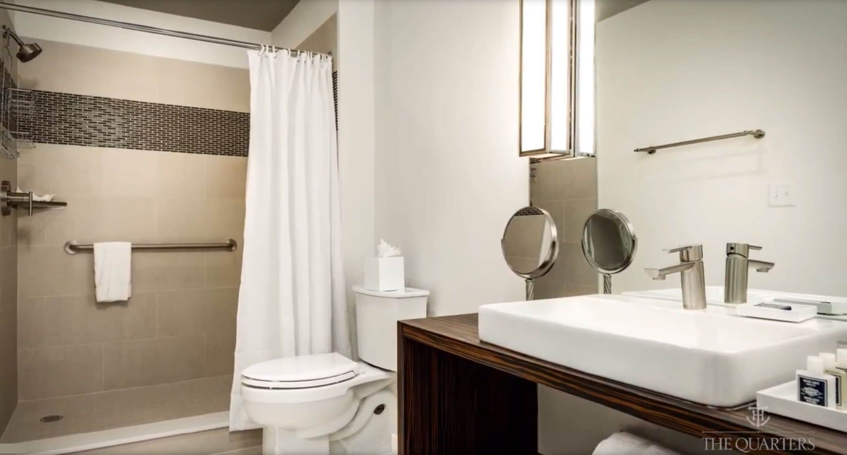Un baño moderno con ducha, inodoro y lavamanos con dos espejos.