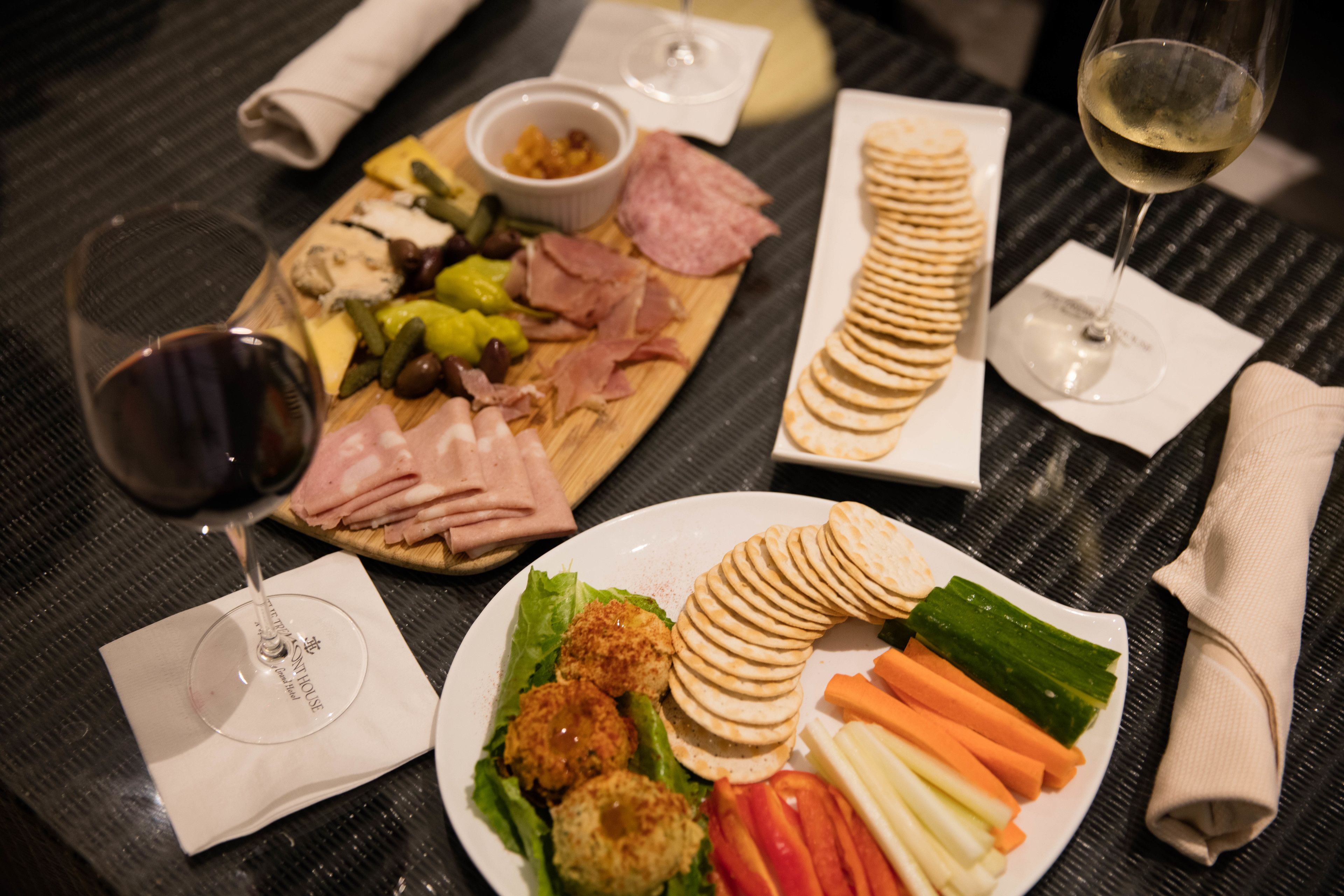 A table with a variety of food items including cheese, meats, crackers, and vegetables, accompanied by wine glasses.