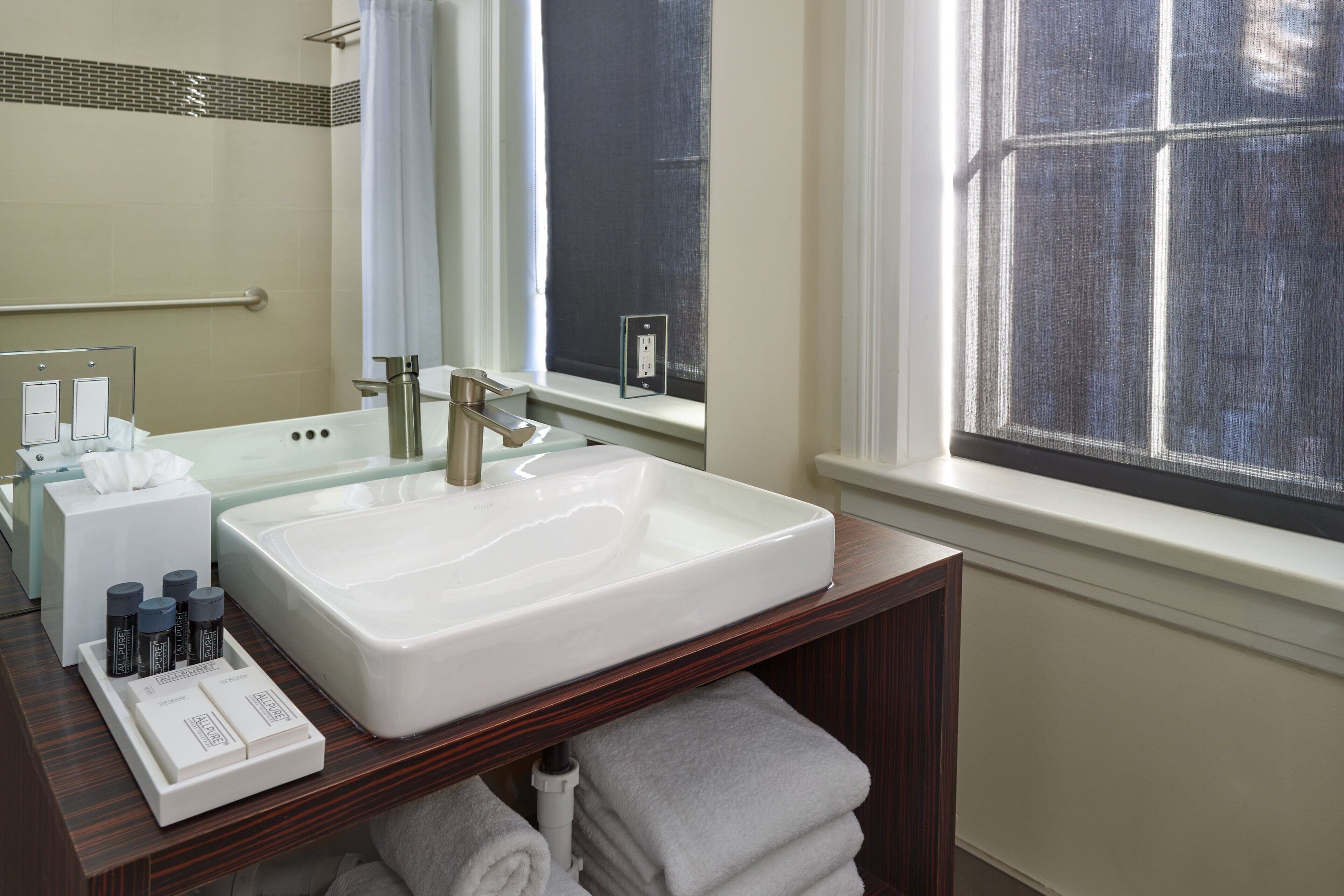 A bathroom with a white sink, a mirror, a towel rack, and a window with a view.