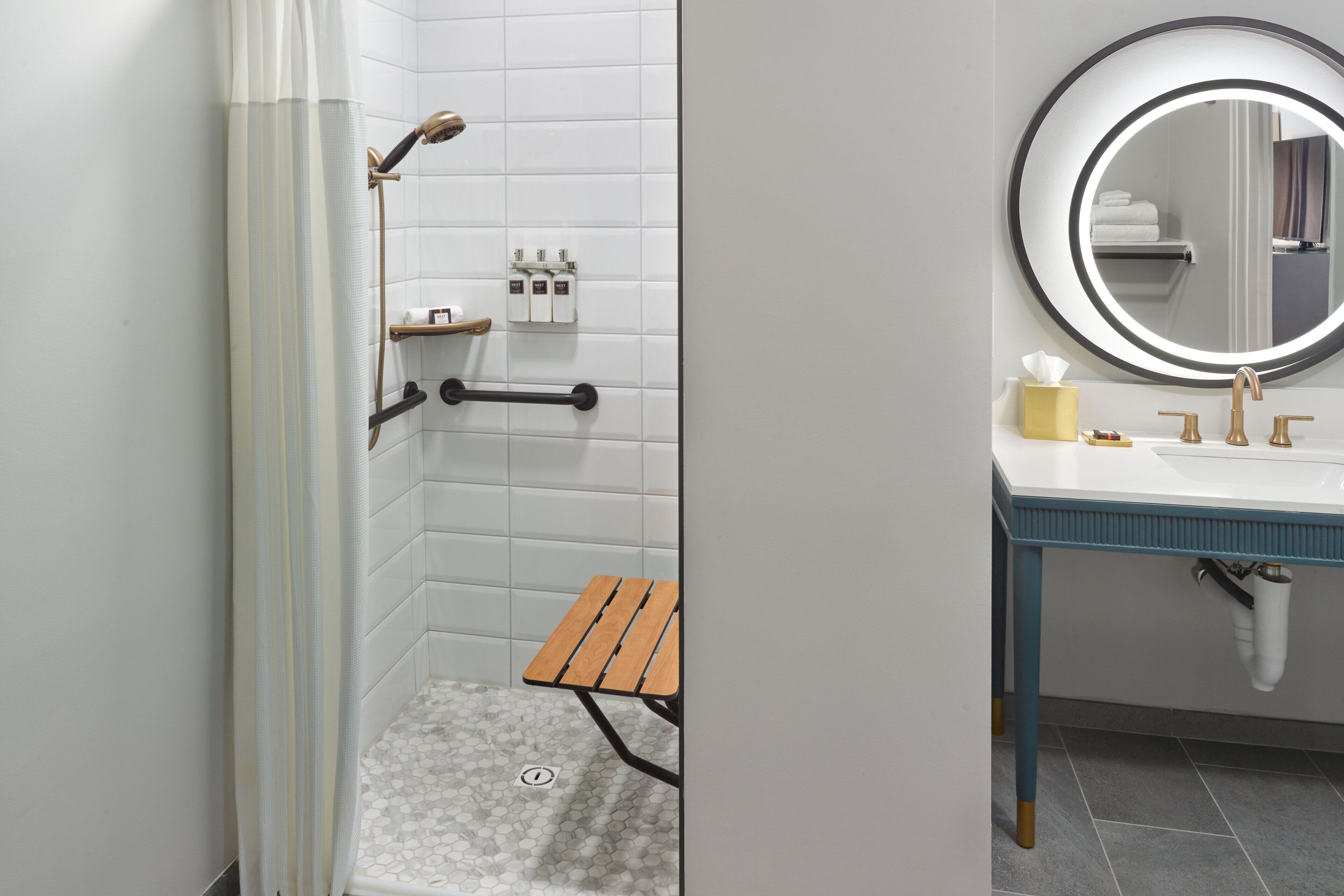 A bathroom with a shower, a sink, a mirror, and a small wooden stool.