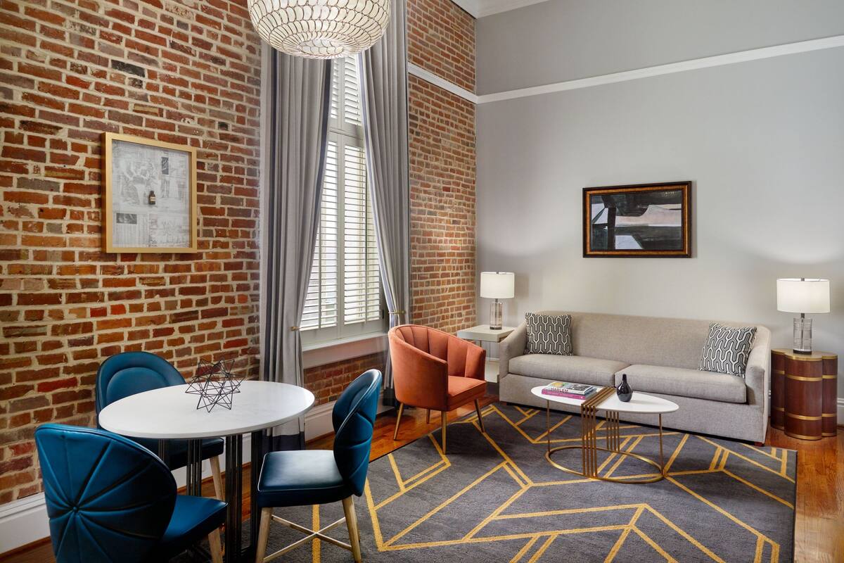 A modern living room with a brick wall, a round table with chairs, a sofa, and a patterned rug.