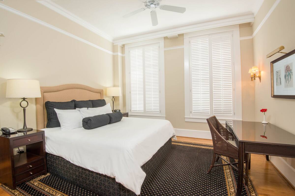 A hotel room with a bed, bedside table, lamp, desk, chair, and a ceiling fan.