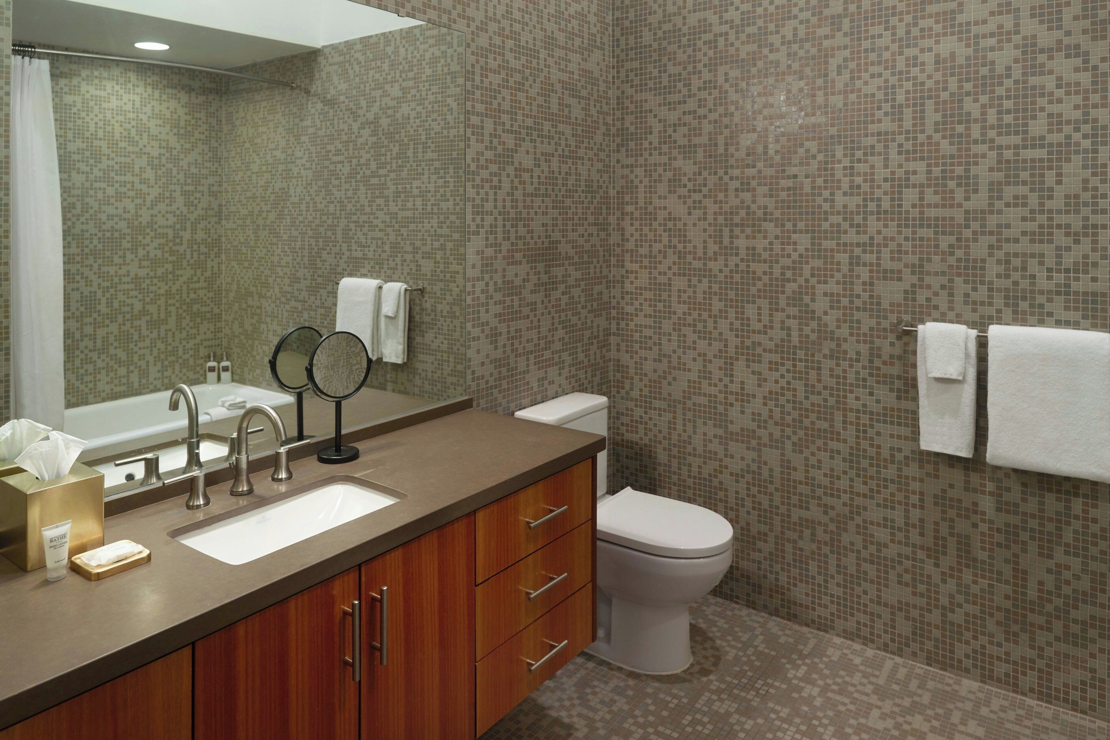 Un baño con lavamanos, espejo, inodoro y paredes de azulejos.