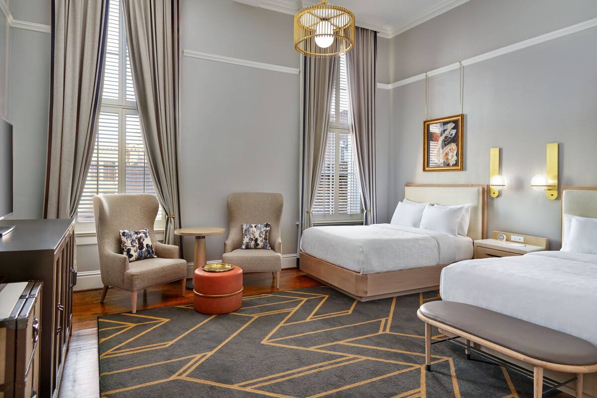 A hotel room with two beds, a sofa, a chair, a small table, and a decorative rug.