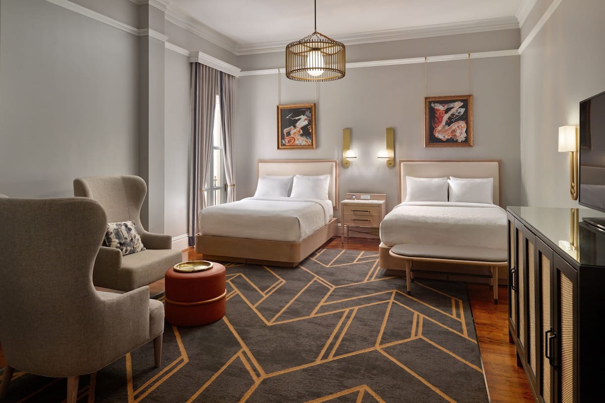 A hotel room with two beds, a sofa, a TV, and artwork on the walls.