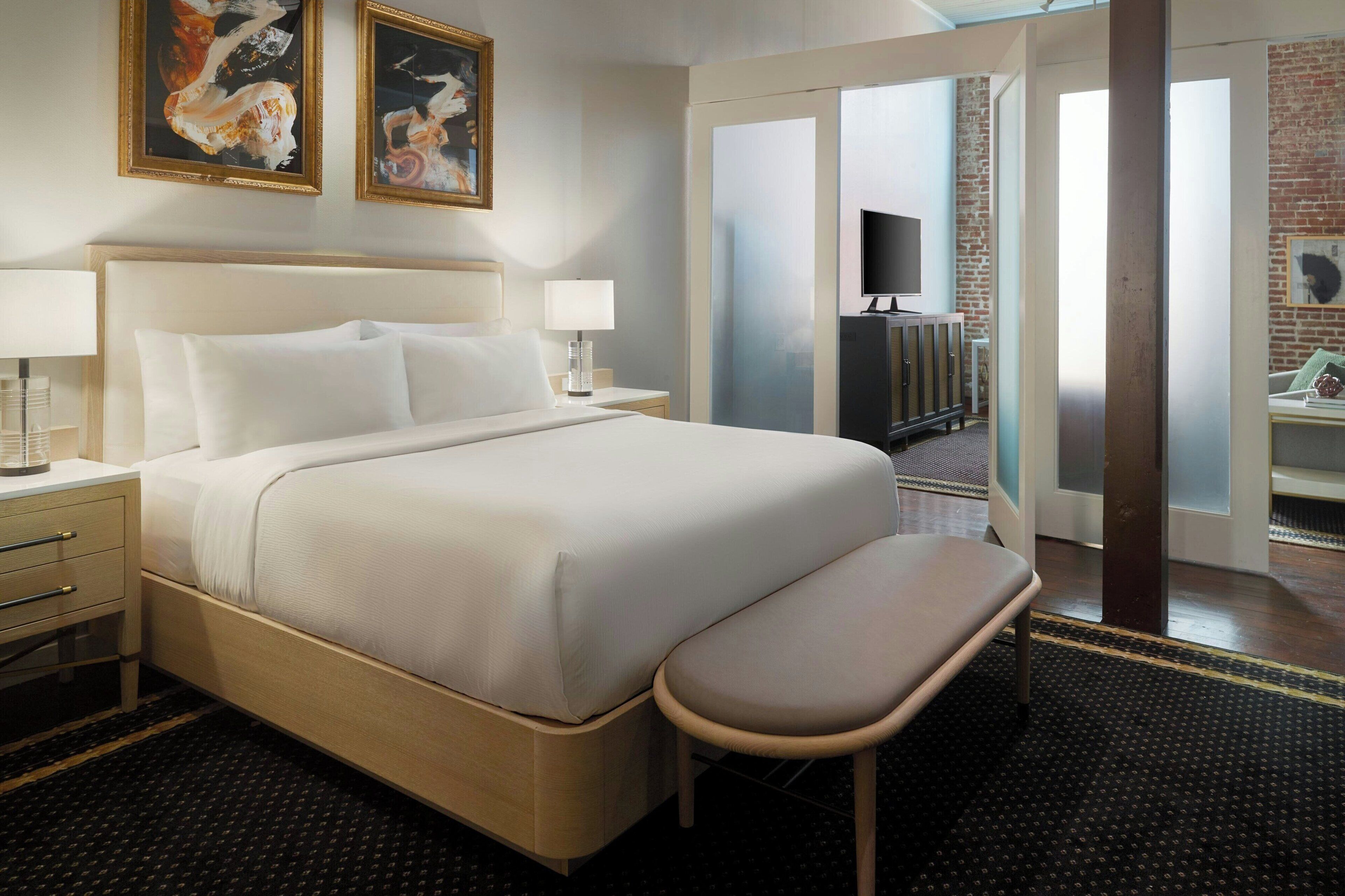 A hotel room with a large bed, bedside tables, a bench, and a TV.