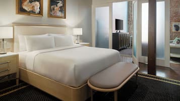 A hotel room with a large bed, bedside tables, a bench, and a TV.