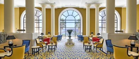 Un vestíbulo de hotel con grandes columnas, ventanas en arco y una alfombra estampada.