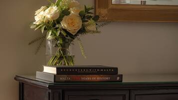 A desk with a vase of flowers, two books titled 'Encounters with Malta' and 'Malta 7000 Years of History,' and a mirror above the desk.