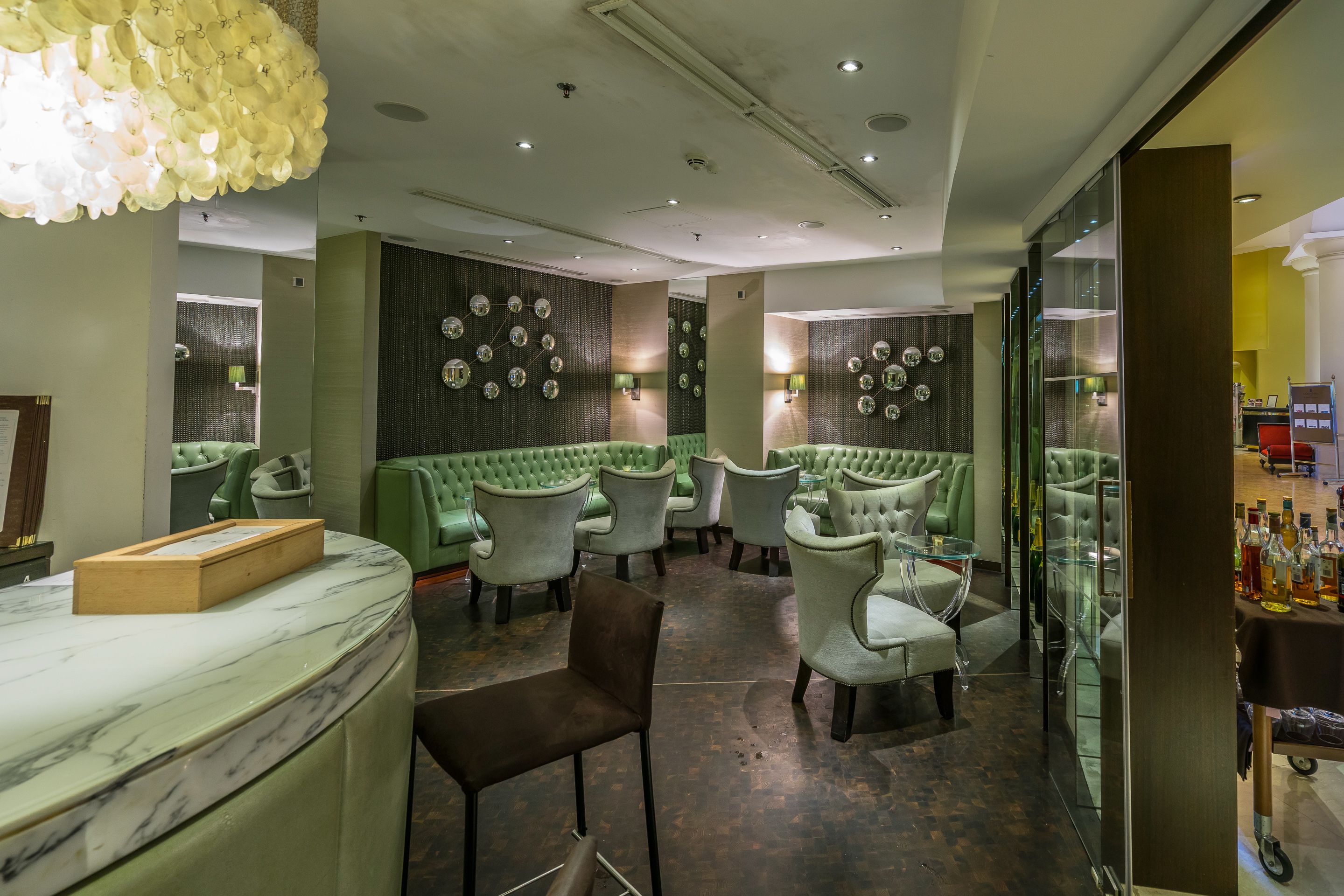 A modern bar area with green upholstered seating, a marble counter, and decorative wall mirrors.