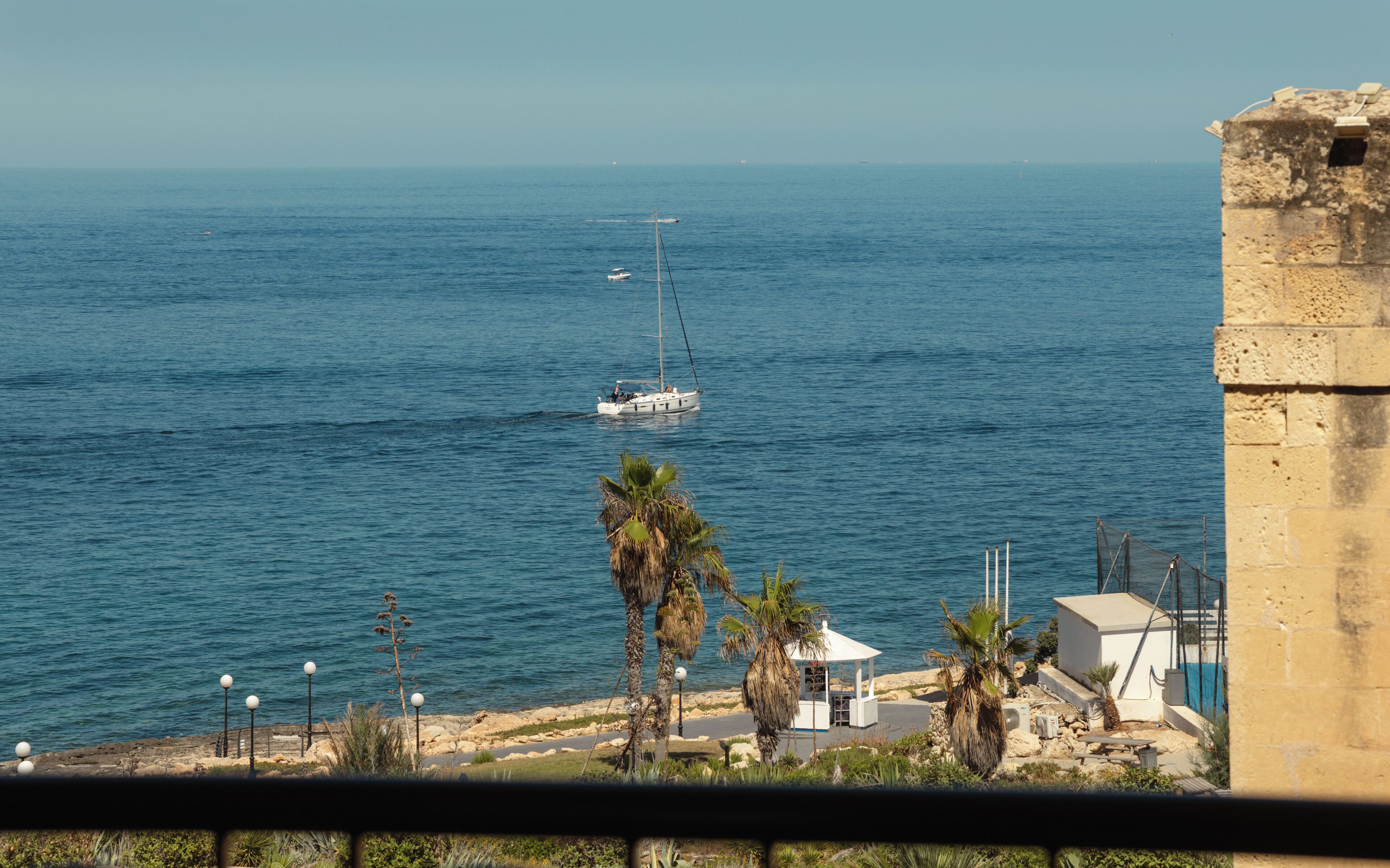 Vista costera con un velero, palmeras y un edificio de piedra.