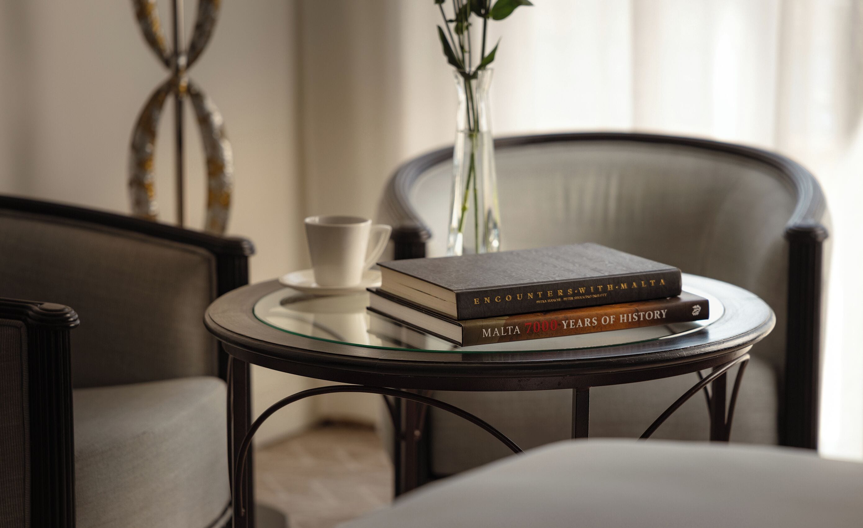A round glass table with two books and a white cup.