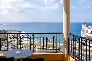 Enjoy the ocean view from this balcony with a table and chairs, overlooking the beach and palm trees.